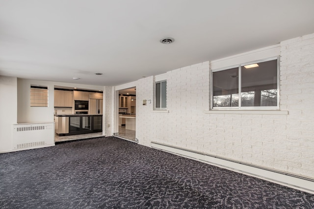 unfurnished living room featuring radiator heating unit, carpet floors, brick wall, and a baseboard heating unit