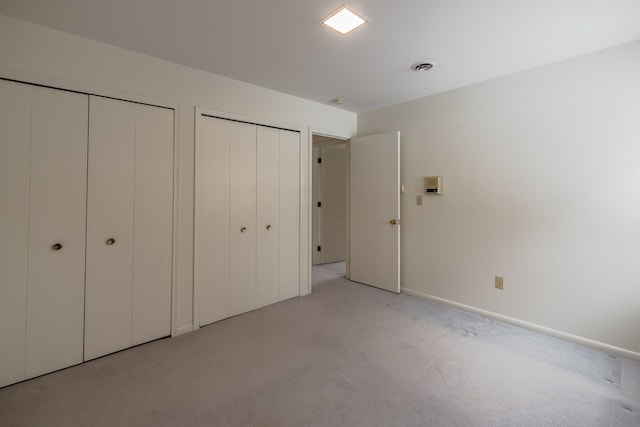 unfurnished bedroom featuring light colored carpet and multiple closets