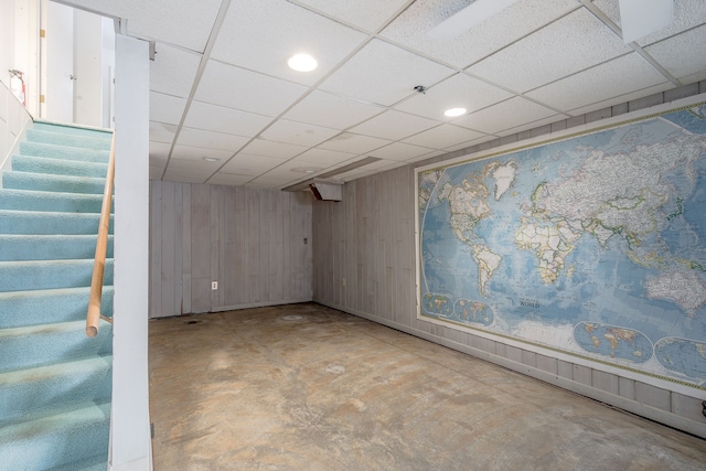 basement featuring a paneled ceiling and wood walls