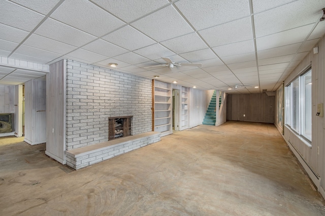 basement with a paneled ceiling, built in shelves, ceiling fan, and a fireplace