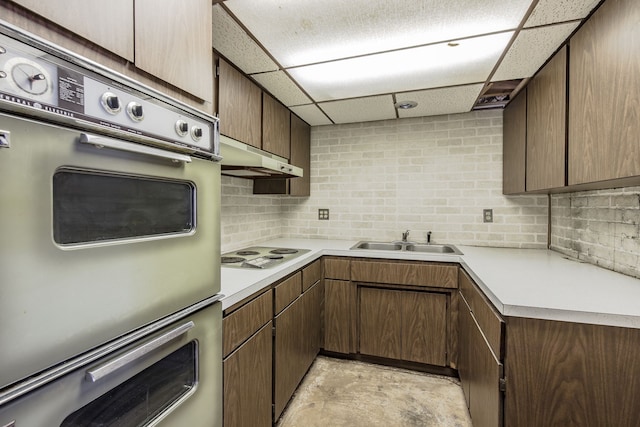 kitchen with sink, white stovetop, double oven, a paneled ceiling, and decorative backsplash