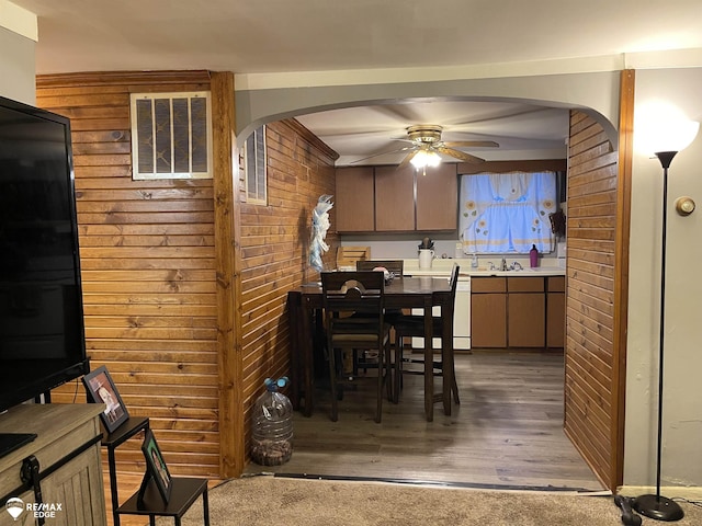 dining room featuring wood walls, ceiling fan, and dark hardwood / wood-style floors