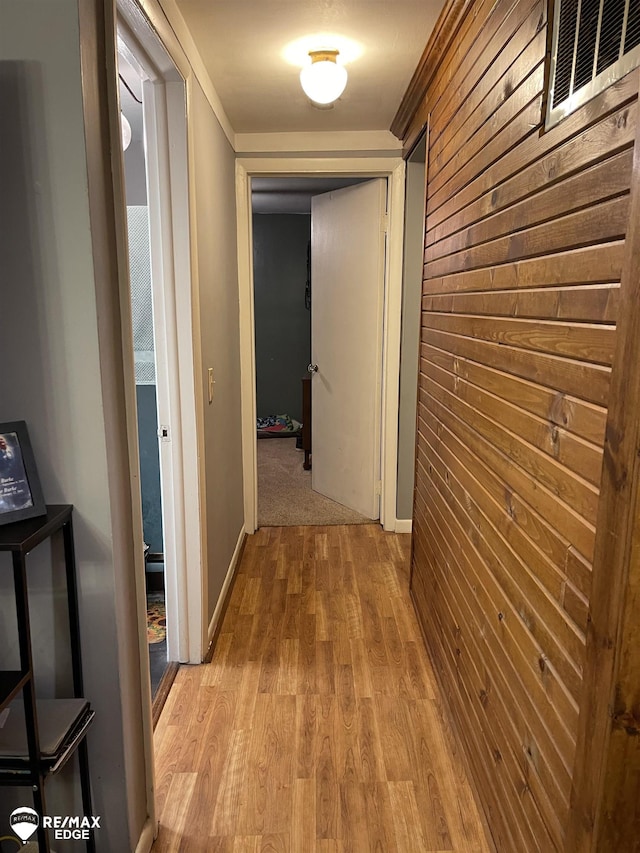 hallway with light wood-type flooring and wooden walls