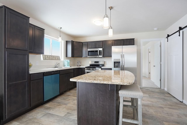 kitchen with decorative light fixtures, a kitchen breakfast bar, a kitchen island, a barn door, and appliances with stainless steel finishes