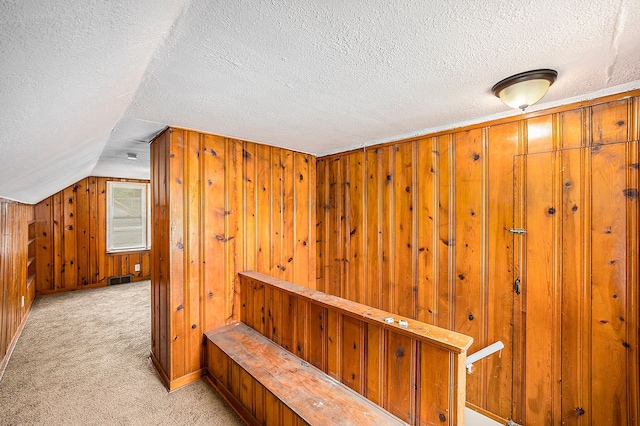 interior space with lofted ceiling, light carpet, wood walls, and a textured ceiling