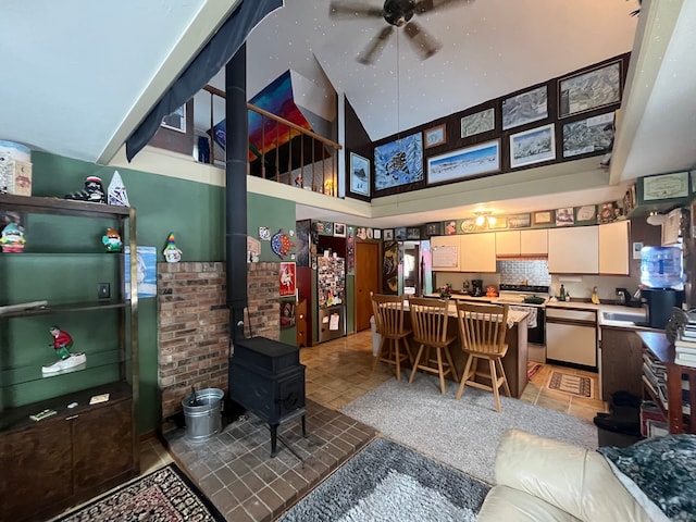 interior space with a towering ceiling, ceiling fan, a wood stove, and sink