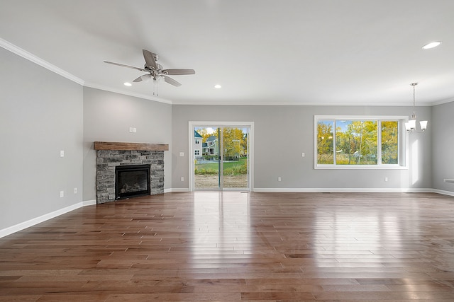 unfurnished living room featuring a fireplace, crown molding, plenty of natural light, and ceiling fan with notable chandelier