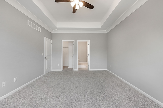 unfurnished bedroom featuring a raised ceiling, connected bathroom, ceiling fan, and carpet