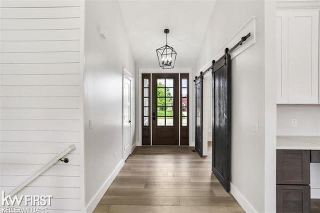 entryway with dark hardwood / wood-style floors, a barn door, a chandelier, and vaulted ceiling