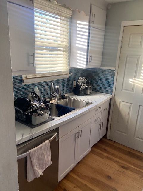 kitchen featuring white cabinets, tasteful backsplash, stainless steel dishwasher, and sink