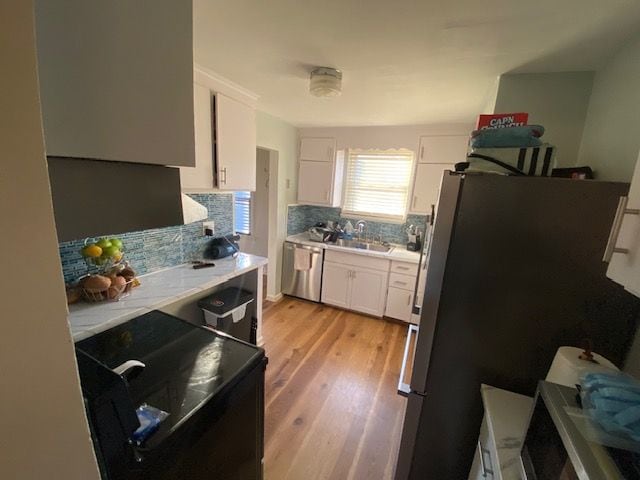 kitchen featuring white cabinetry, sink, light hardwood / wood-style flooring, backsplash, and appliances with stainless steel finishes