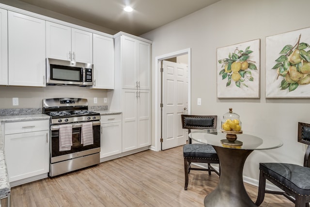 kitchen featuring white cabinetry, stainless steel appliances, light stone counters, and light wood-type flooring