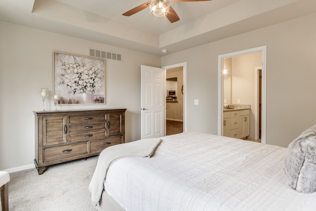 carpeted bedroom featuring a raised ceiling, connected bathroom, and ceiling fan