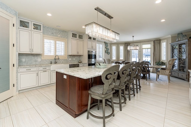 kitchen featuring a center island, a notable chandelier, light stone counters, sink, and decorative light fixtures