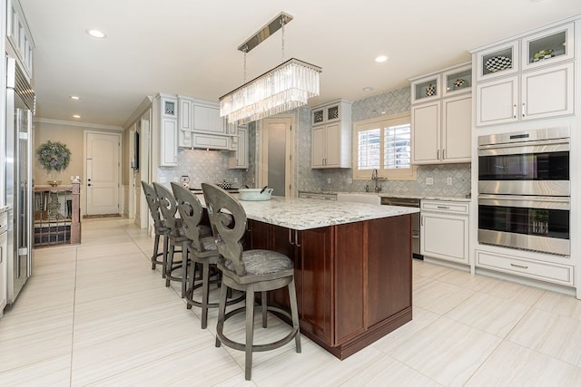 kitchen with stainless steel appliances, a center island, hanging light fixtures, light stone countertops, and a notable chandelier