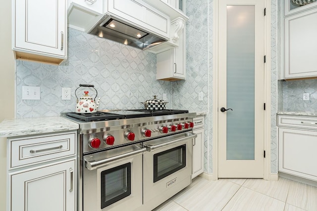 kitchen featuring custom exhaust hood, double oven range, white cabinetry, and light stone counters