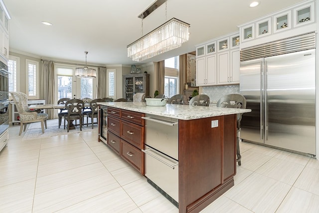 kitchen with built in fridge, a center island, a kitchen bar, white cabinetry, and decorative light fixtures