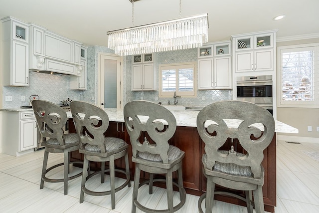 kitchen with crown molding, stainless steel double oven, light stone counters, a kitchen island, and white cabinetry