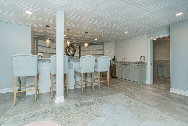 kitchen with pendant lighting, a kitchen bar, gray cabinets, and light stone countertops