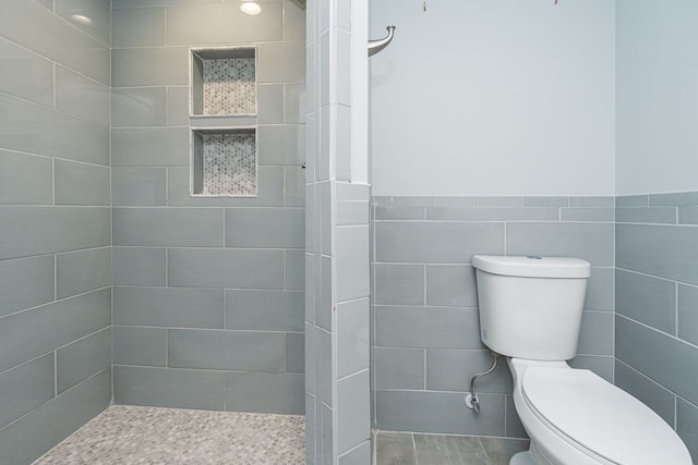 bathroom featuring toilet, a tile shower, and tile walls