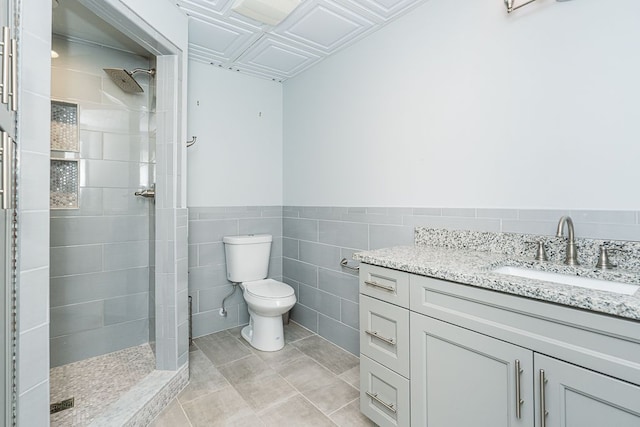 bathroom featuring tile patterned flooring, tile walls, a tile shower, toilet, and vanity