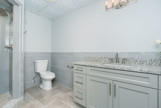 bathroom with toilet, tiled shower, tile walls, tile patterned floors, and vanity