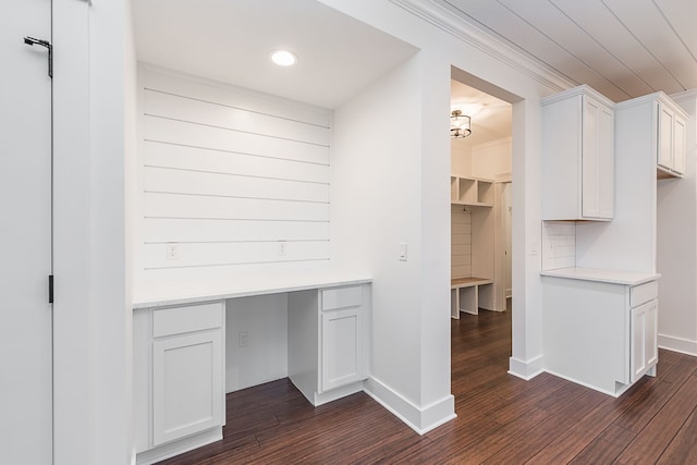 unfurnished office with crown molding, built in desk, and dark wood-type flooring