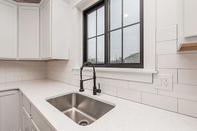 kitchen featuring white cabinets, backsplash, light stone counters, and sink