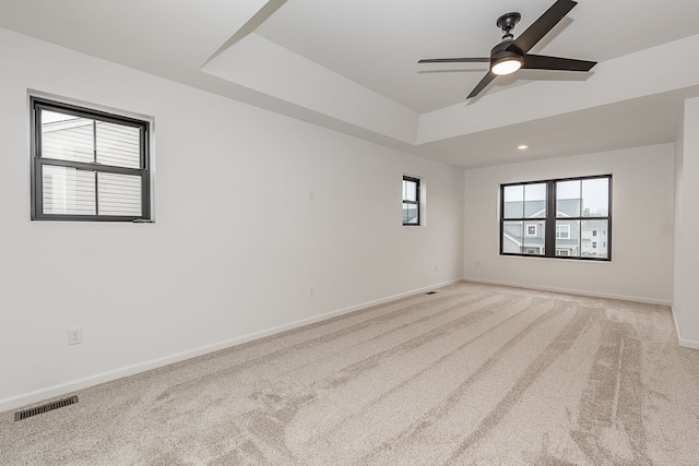 empty room with light carpet, a tray ceiling, and ceiling fan