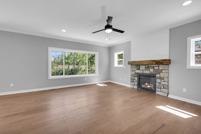 unfurnished living room with ornamental molding, a stone fireplace, ceiling fan, and light wood-type flooring