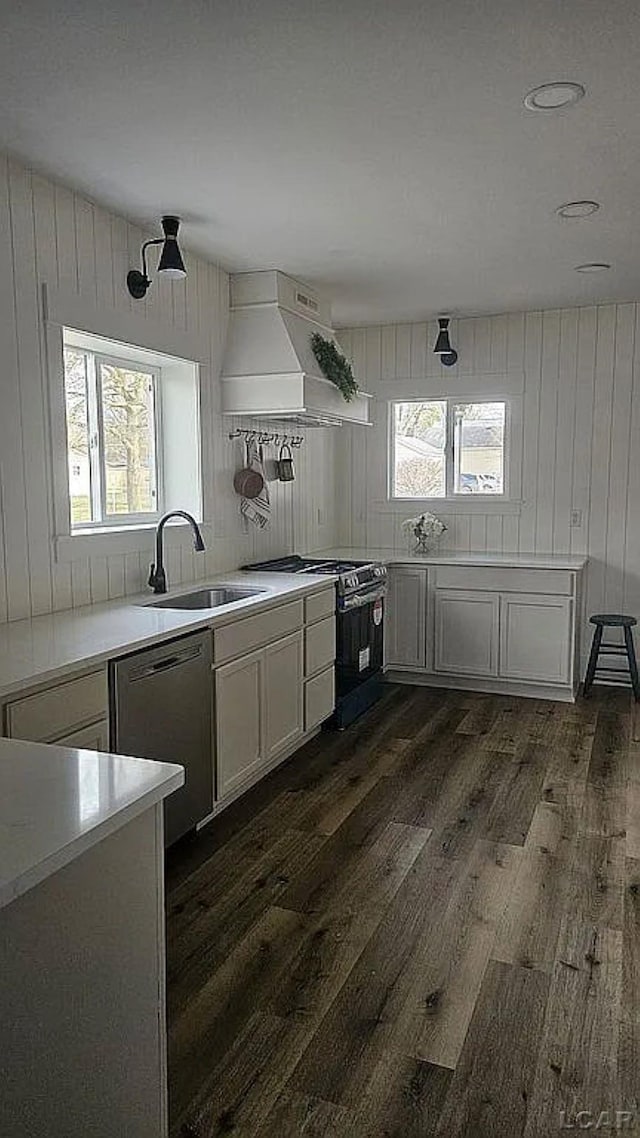 kitchen featuring premium range hood, stainless steel dishwasher, black gas range oven, sink, and dark hardwood / wood-style floors