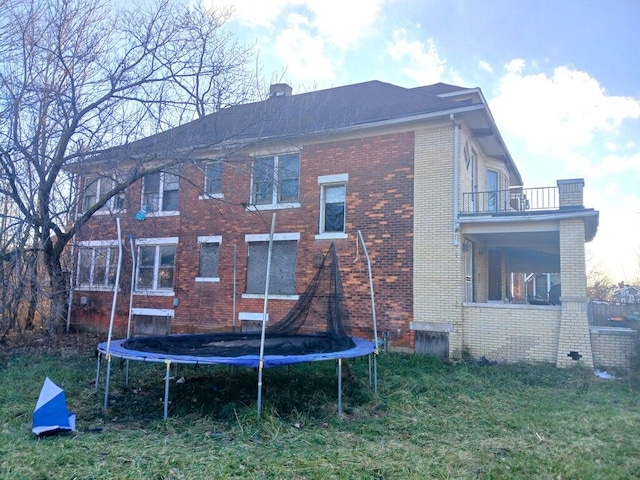 rear view of house with a balcony, a yard, and a trampoline