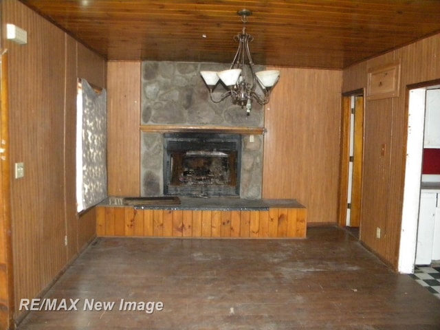 unfurnished living room with wood ceiling, dark wood-type flooring, a notable chandelier, a fireplace, and wood walls