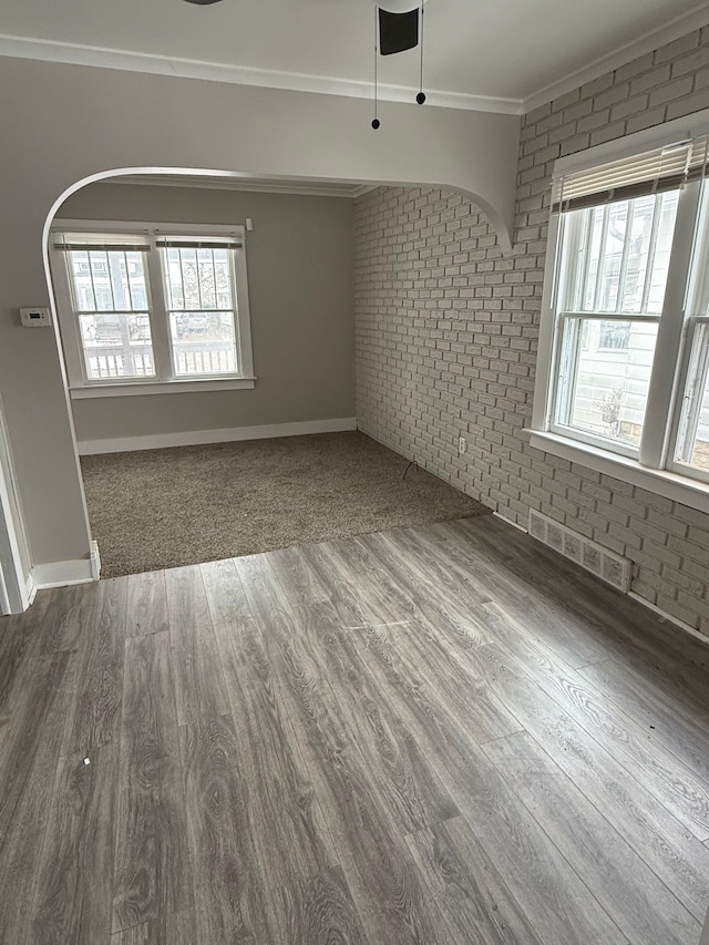 empty room with hardwood / wood-style flooring, brick wall, and ornamental molding