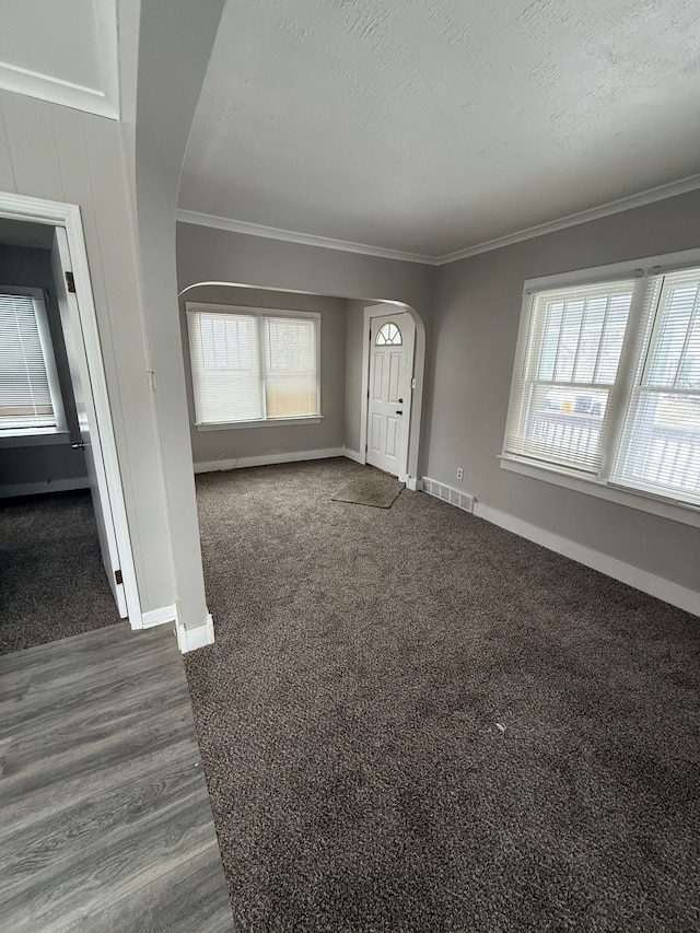 entrance foyer with dark colored carpet, a healthy amount of sunlight, ornamental molding, and a textured ceiling