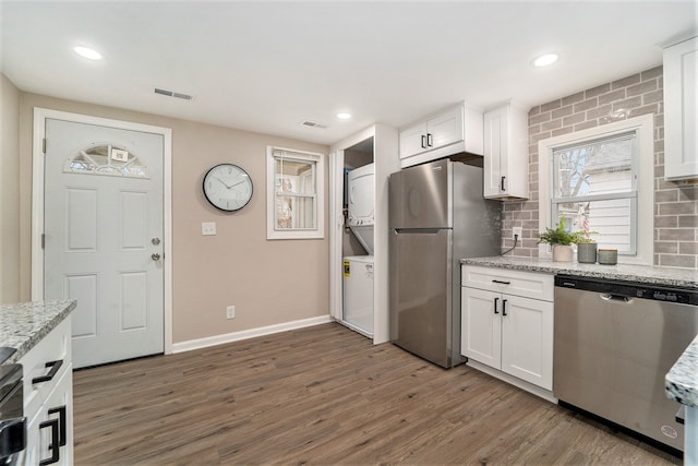 kitchen featuring stacked washer / drying machine, light stone countertops, white cabinets, and appliances with stainless steel finishes