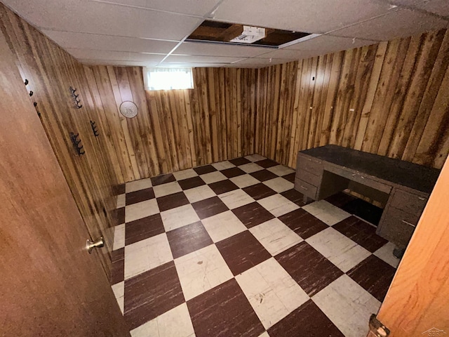 basement featuring a drop ceiling and wood walls