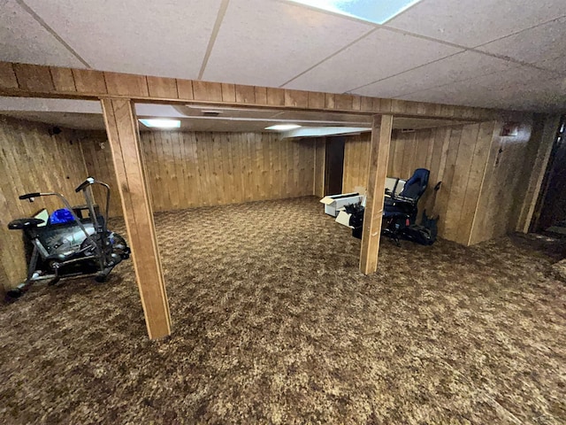 basement with a drop ceiling, carpet floors, and wooden walls