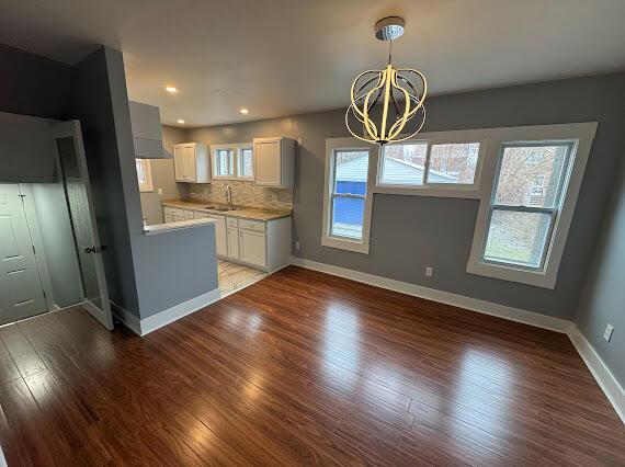 kitchen with sink, tasteful backsplash, a notable chandelier, hardwood / wood-style floors, and white cabinets