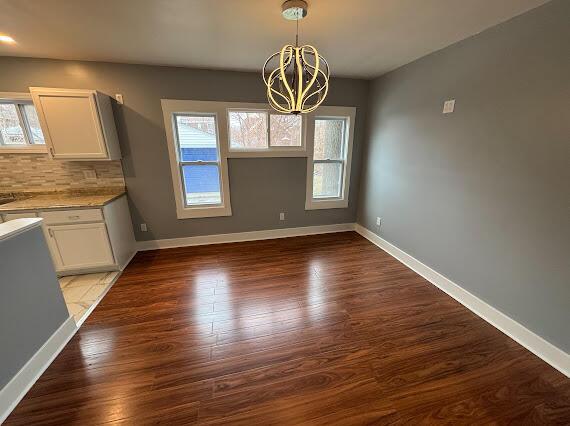 unfurnished dining area with a chandelier and dark wood-type flooring