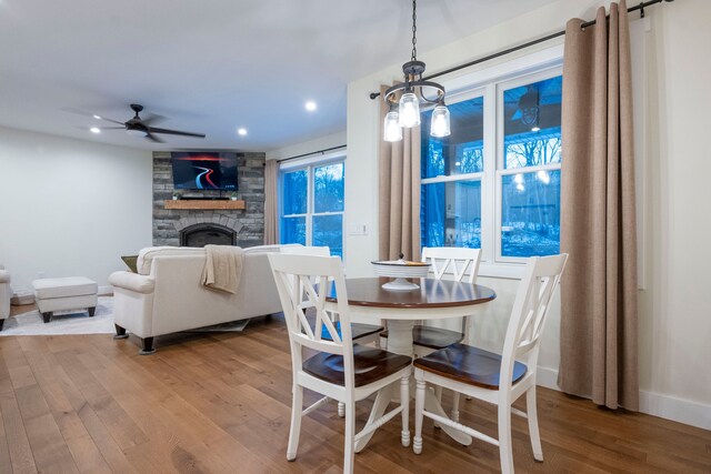 dining space with ceiling fan, a stone fireplace, and wood-type flooring