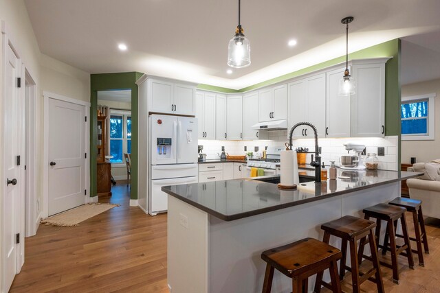 kitchen featuring white cabinetry, a kitchen bar, kitchen peninsula, hanging light fixtures, and white refrigerator with ice dispenser