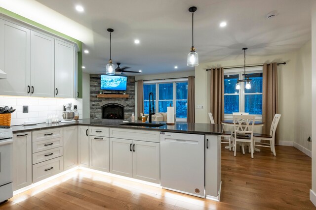 kitchen featuring sink, white cabinetry, white appliances, hanging light fixtures, and a stone fireplace