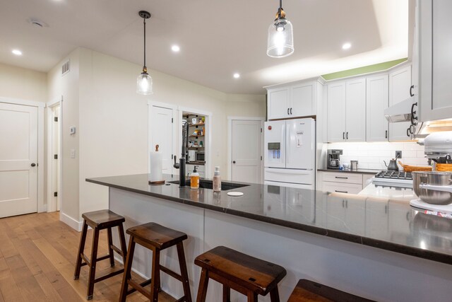 kitchen featuring white cabinets, pendant lighting, white refrigerator with ice dispenser, and sink