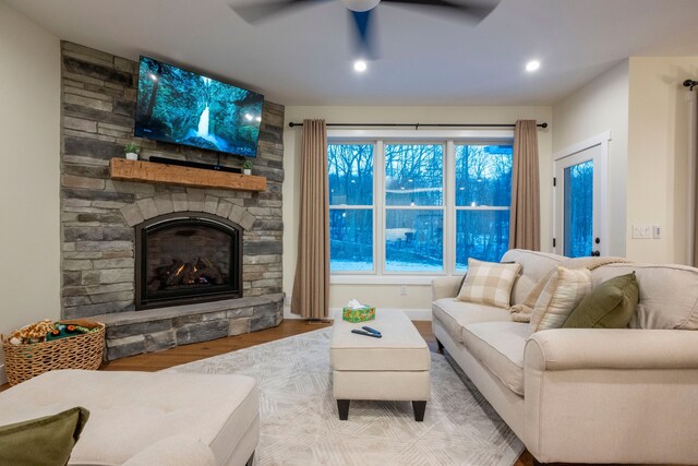 living room featuring ceiling fan, light hardwood / wood-style flooring, and a stone fireplace