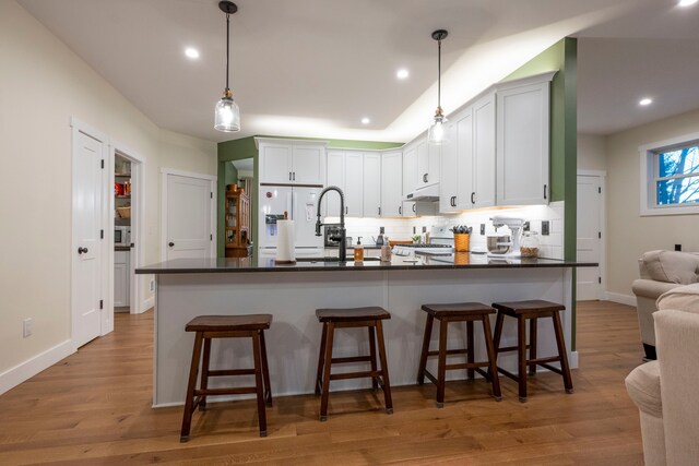 kitchen featuring a kitchen breakfast bar, hardwood / wood-style floors, pendant lighting, white cabinets, and tasteful backsplash