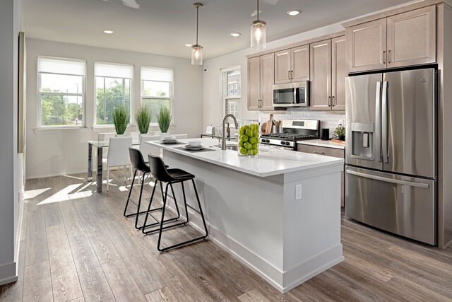 kitchen with pendant lighting, a center island with sink, decorative backsplash, light wood-type flooring, and appliances with stainless steel finishes