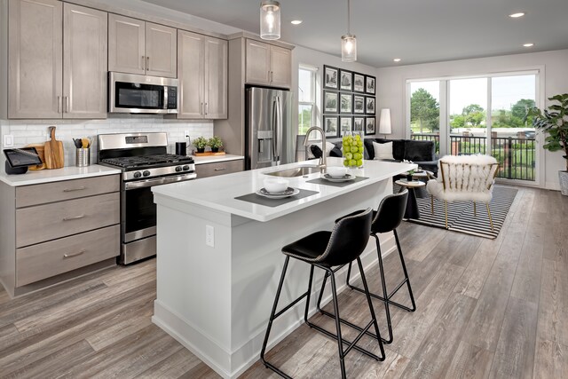 kitchen featuring appliances with stainless steel finishes, a center island with sink, gray cabinets, and hanging light fixtures