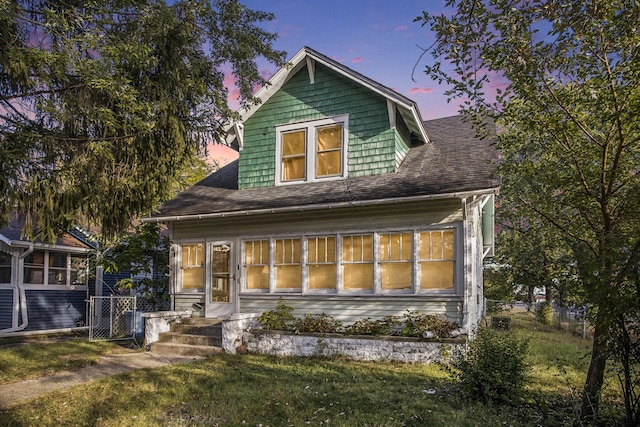 back house at dusk with a lawn and a sunroom