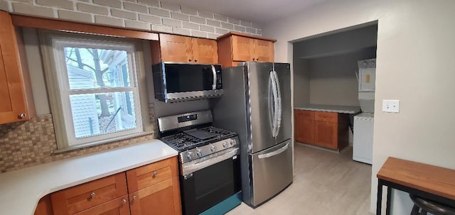 kitchen with stacked washer and dryer, decorative backsplash, brown cabinets, stainless steel appliances, and light countertops